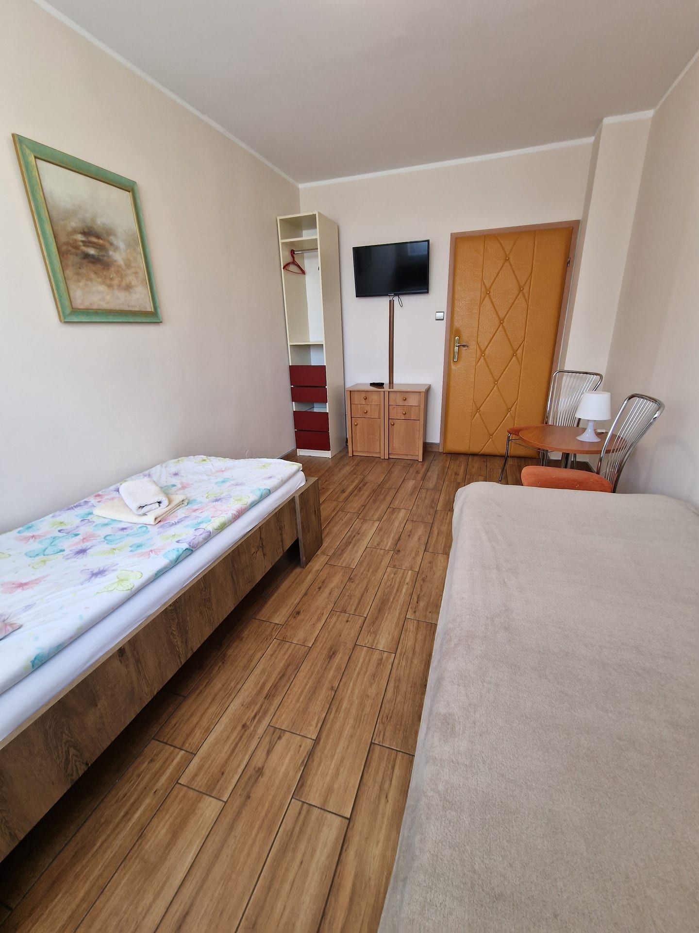 Pokój 2-osobowy - łóżko z kolorową pościelą, szafa z czerwonymi szufladami, telewizor i drzwi wejściowe - Zdjęcie 4